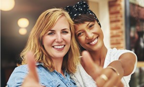 two women holding a thumbs up to the camera